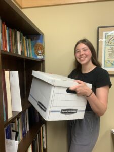 A young woman holds a box of files in the Archives for an article on home archival tips